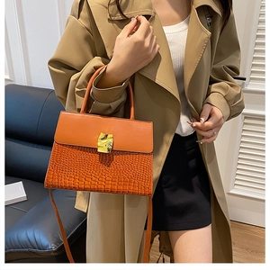 Détail du sac à main orange motif crocodile avec boucle dorée porté par un mannequin chic