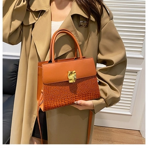 Orange croc-embossed handbag with gold buckle styled on a trench coat model