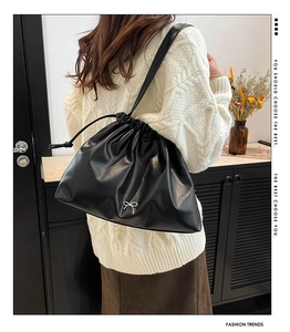 Detail of black drawstring shoulder bag with silver bow accent and soft leather texture