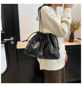 Detailed side view of black drawstring crossbody bag with delicate metal bow ornament
