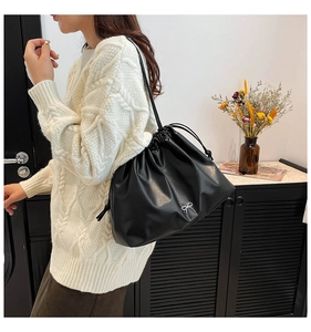 Detail of black pleated shoulder bag with silver bow accent and drawstring closure