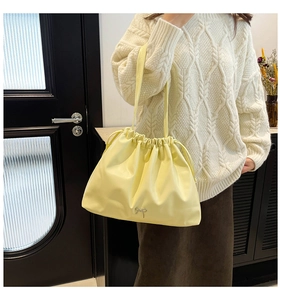 Detail of a bright yellow drawstring tote bag featuring a delicate metal bow accent