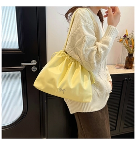 Close-up of a pale yellow pleated cloud bag with a silver bow on a shoulder strap