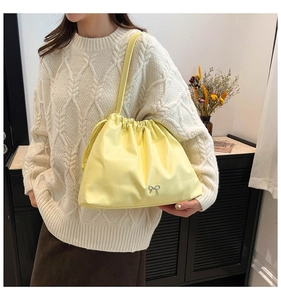 Detail of light yellow pleated bucket bag featuring a silver metal bow and drawstring closure