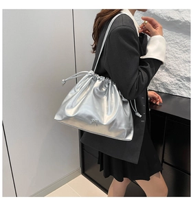Silver metallic drawstring shoulder bag with bow detail shown on a model in a modern setting