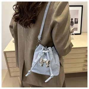 Close-up of light blue drawstring bucket bag with silver bow accent on a shoulder strap