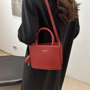 Sac à main carré rouge avec lettrage doré porté par un mannequin en manteau noir
