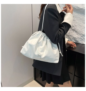 Detail of the white drawstring shoulder bag featuring a silver metal bow decoration