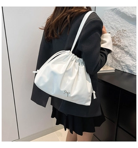 Close-up of white drawstring shoulder bag featuring a silver metal bow detail