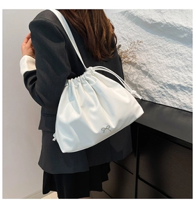 Detail of white drawstring bucket bag with silver bow accent on a model's shoulder