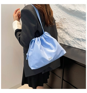 Detail of light blue pleated bucket bag with silver bow and drawstring on grey jacket