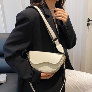 Cream vintage saddle bag with wide strap worn by model in a minimalist indoor setting
