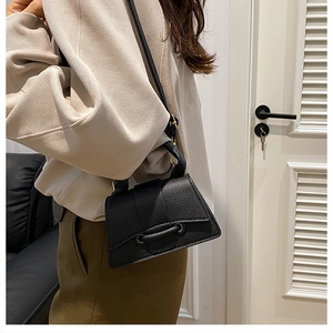 Détail d'un sac à main noir en cuir litchi avec fermoir doré porté à l'épaule