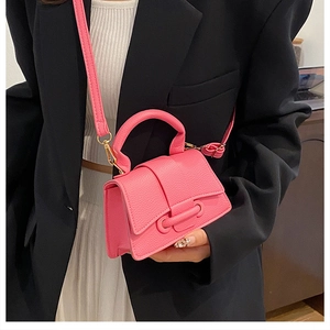 Mini sac à main rose texture litchi avec détails dorés porté sur un blazer noir