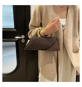 Detail of a dark brown crocodile pattern handbag featuring a gold sculptural metal handle