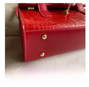 Macro view of red crocodile-embossed leather handbag showing durable metal base studs