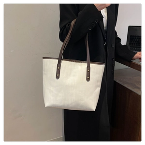 Dettaglio della borsa tote in tela bianca con manici in pelle marrone e borchie in metallo