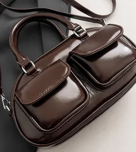 Détail du sac baguette marron foncé brillant avec deux poches avant et matériel argenté