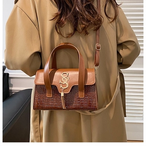 Detail view of caramel faux leather bag with crocodile texture and gold 'S' pendant