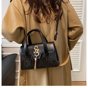 Detail of black crossbody bag with crocodile texture, gold SS logo and tassel