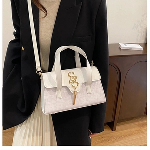 Detail view of white handbag with crocodile texture, gold double S buckle and tassel ornament