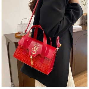 Detail of red croc-embossed handbag with gold logo tassel shown in lifestyle setting