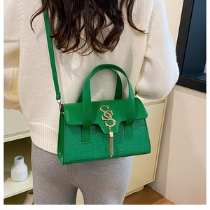 Model wearing a green textured shoulder bag with golden S-buckle and elegant tassel detail