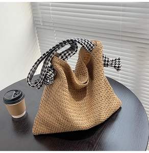 Detail of woven straw bucket bag with stylish houndstooth strap on a wooden table