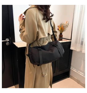 Detailed side view of the black Oxford cloth messenger bag styled on a beige trench coat
