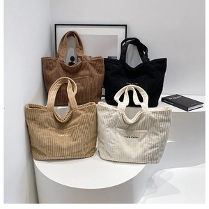 Detail of four colorful corduroy tote bags with Free Color embroidery on a minimalist stand