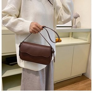 Detail of dark brown matte leather underarm bag with wavy flap design and gold hardware