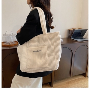 Close-up of white corduroy tote bag featuring 'Free Color' embroidery and large front pocket