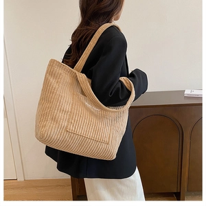 Detail view of corduroy tote bag featuring front pocket and minimalist white text logo