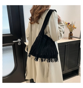 Detail of a black suede fringe shoulder bag styled with a beige trench coat on a model
