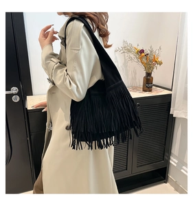 Detail of black suede shoulder bag with long bohemian tassels and wide shoulder strap