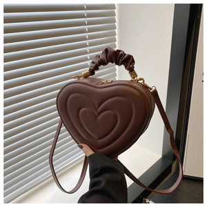 Détail d'un sac marron en forme de cœur avec texture matelassée et poignée plissée