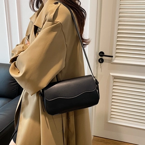 Sac à bandoulière noir élégant avec bord ondulé porté sur un trench-coat kaki classique