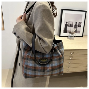 Close-up of vintage plaid wool tote bag with black leather strap and metal ring hardware
