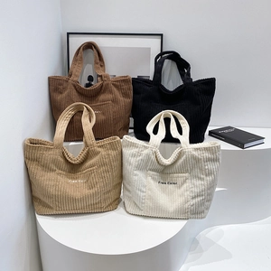 Large corduroy tote bags in four neutral colors displayed on minimalist pedestals