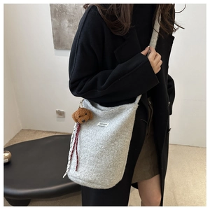 Detail view of grey felt bucket bag with bear charm on black coat background