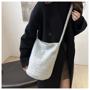 Detail of light grey textured knit bucket bag with minimalist brand label on black coat