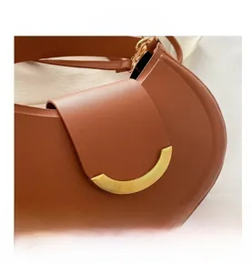 Dettaglio della borsa a mezzaluna in pelle caramello con fibbia metallica dorata a semicerchio