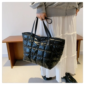 Detail of black quilted tote bag with golden rivets and leather-textured handles