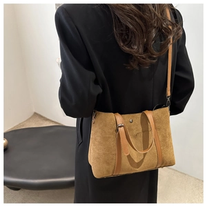 Brown frosted tote bag with leather straps worn over a blazer in a minimalist office setting