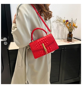 Detail of red croc-embossed leather handbag with gold clasp worn with beige coat