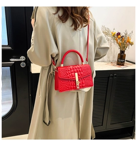 Detailed view of red crocodile embossed crossbody bag worn with a beige trench coat