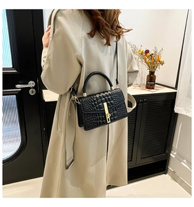Détail d'un sac à main noir texture crocodile avec boucle dorée porté par un modèle