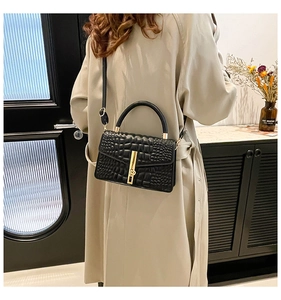 Close-up of black croc-embossed handbag with gold clasp on a beige trench coat