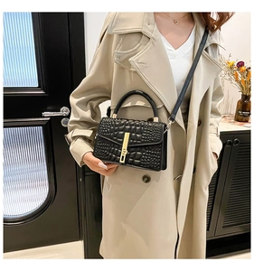 Detail of black crocodile texture handbag with gold buckle held by model in trench coat