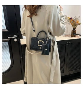 Détail du sac noir à texture crocodile avec boucle dorée et mini pendentif porte-monnaie